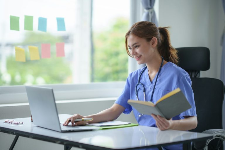 Attentive nurse in scrubs reviewing medical history or patient information on her laptop in office.